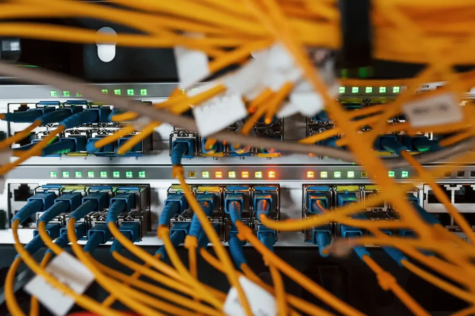 Câbles de fibre optique orange et connecteurs bleus branchés sur les ports d’un commutateur réseau aux diodes vertes