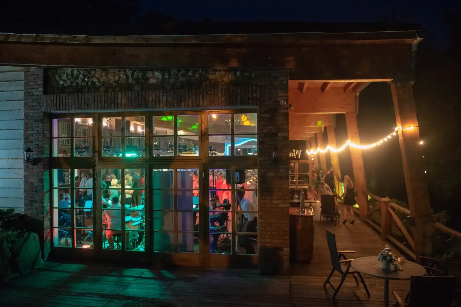 Devanture vitrée d’un commerce éclairée à la tombée de la nuit, guirlande lumineuse et terrasse en bois